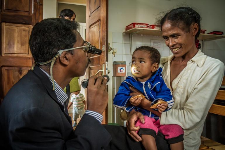 pediatric patient in mother's arms with an ophthamologist who shining light in child's eyes