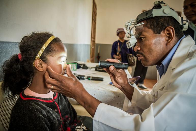 optometrist shining light into and examining a young girl's eyes