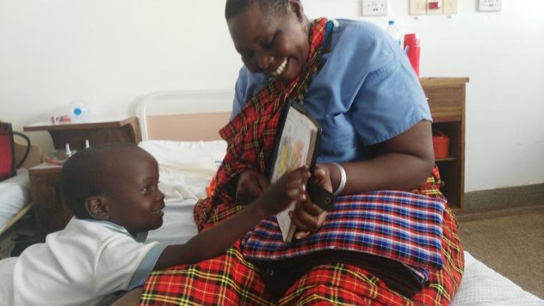 Young boy smiling and reading a book with his caregiver