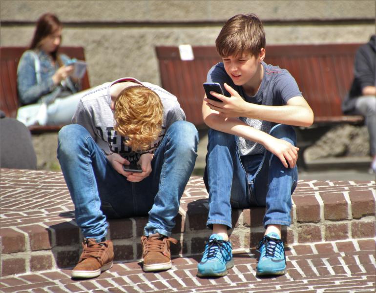 two young boys sitting and looking at their cellphones