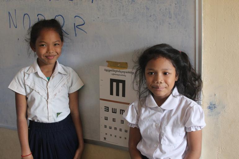 Two young girls in school uniforms standing in front of eye chart