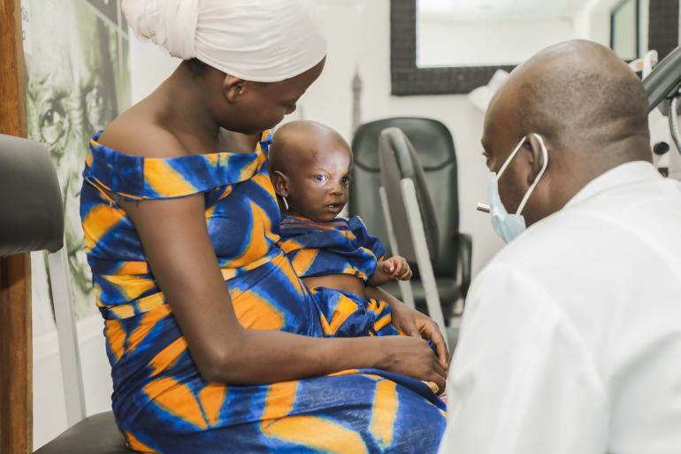 Baby Jojo in Burundi sitting in mother's lap being examined by ophthalmologist by Jean de Dieu