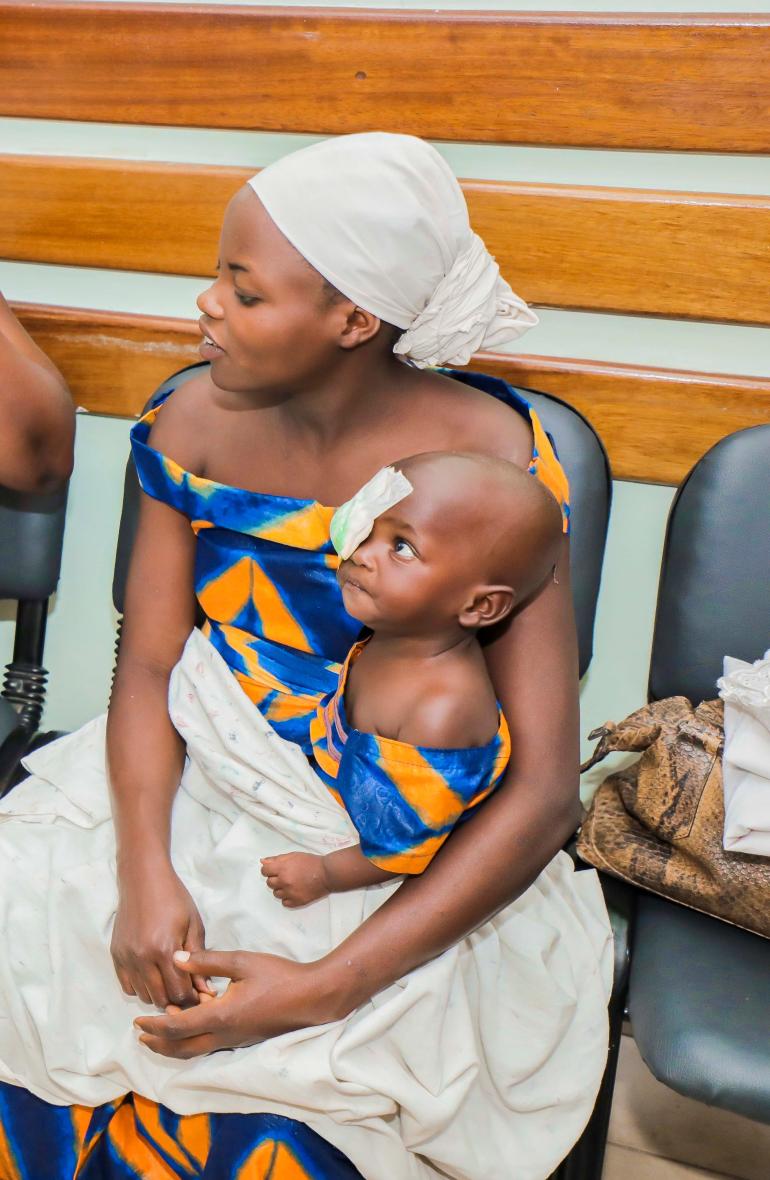 Jojo in Burundi with eye patch sitting in her mother's lap.