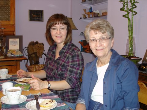 Two women sitting at table with coffee and bread looking at camera smiling