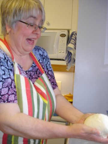 woman in apron smiling while holding loaf of round bread