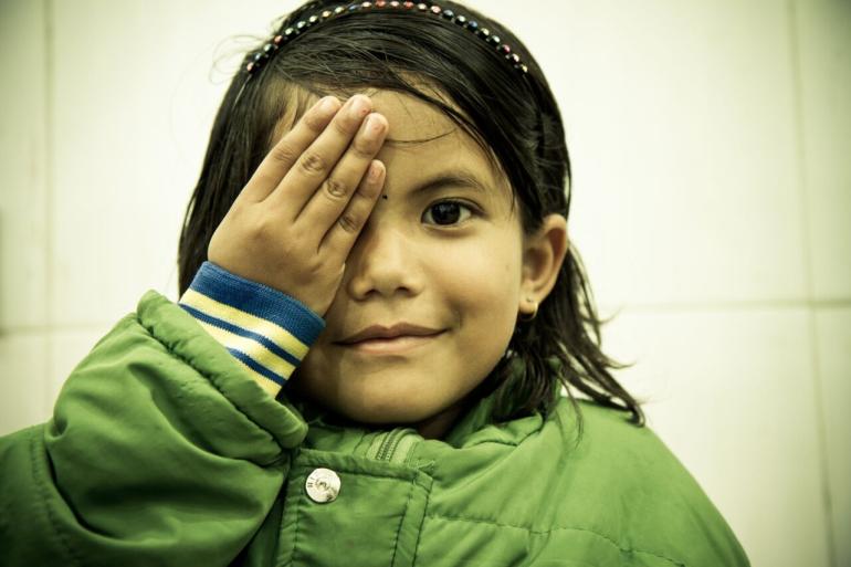 Young Nepali girl looking at camera and holding right hand over right eye 