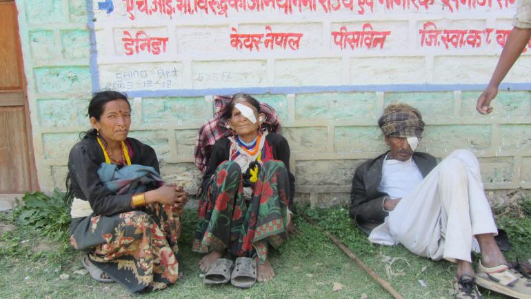 group of three patients sitting outside and looking towards camera, two with bandages over one eye