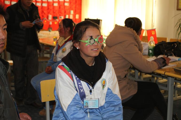 Dolkar, a Tibetan student in her school uniform having an eye examination done while wearing green glasses