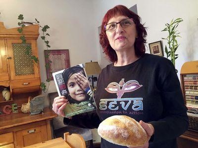 Pat smiling at camera while holding a Seva gift of sight catalogue and loaf of bread