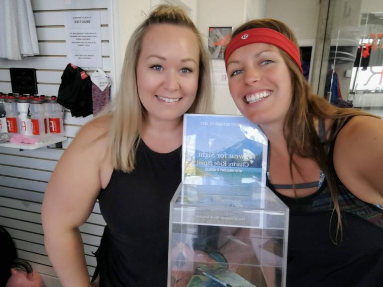 Ashlee and Mallory holding up their donation box for their spin class