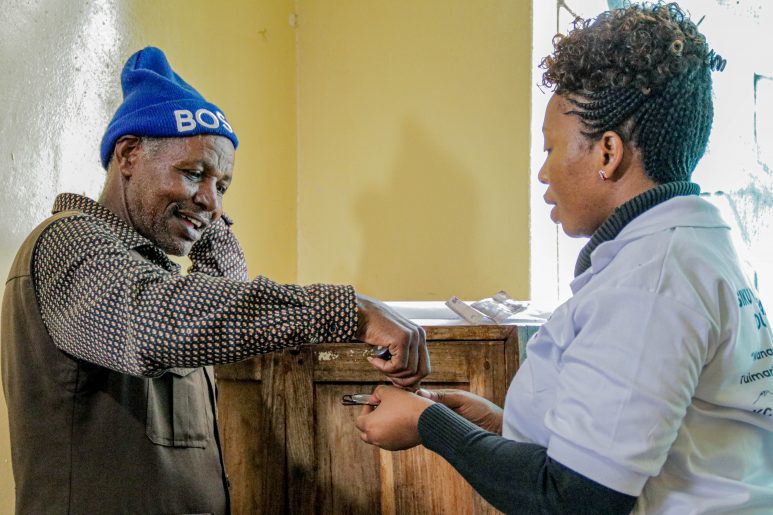 Nurse Faraja helping a male patient with their glasses.