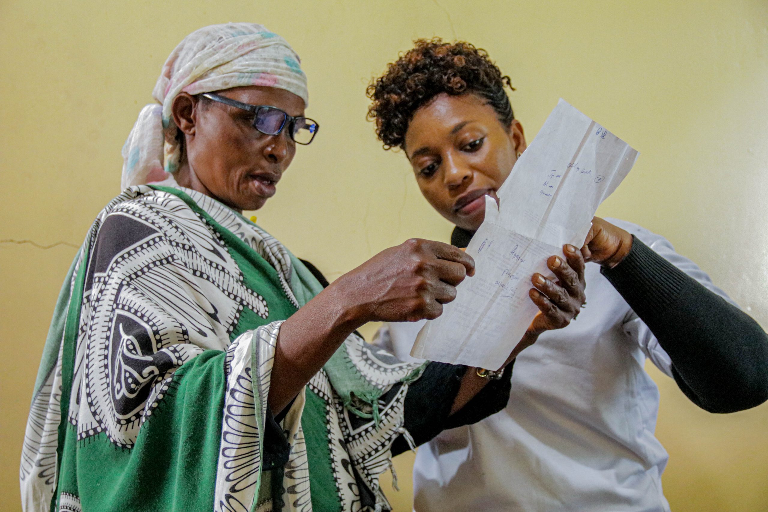 Nurse Faraja helping a female patient with their glasses.