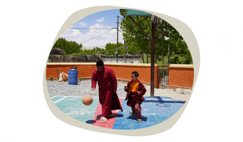 Nepali teen with glasses playing basketball with a younger peer